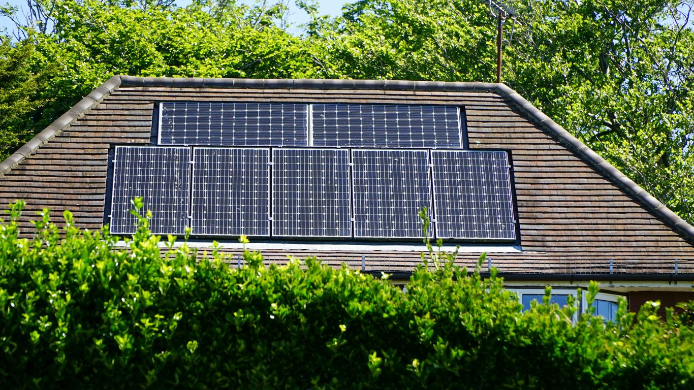 Solar panels on a residential roof surrounded by greenery, illustrating energy efficiency and home improvement benefits.