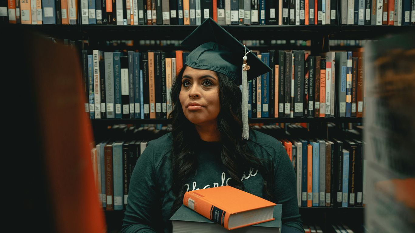 a woman in a cap and gown holding a stack of books