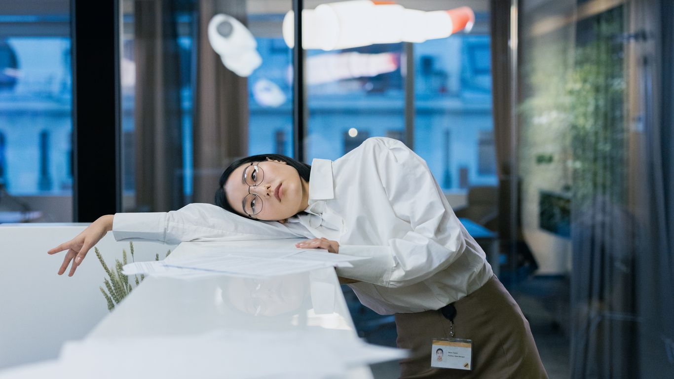Person in office leans on desk, appearing tired or bored.