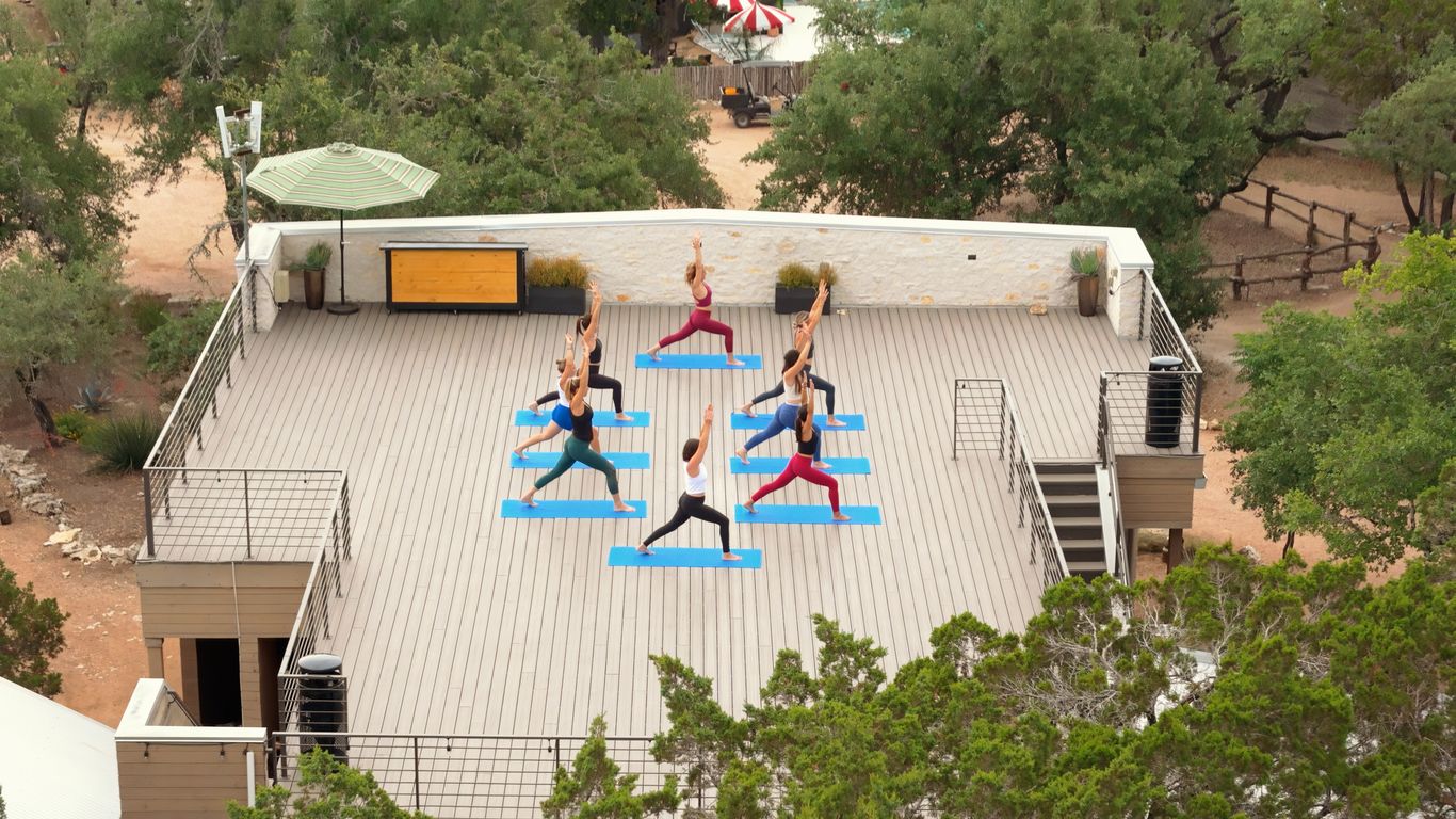 Group of people practicing yoga on a wooden deck outdoors.