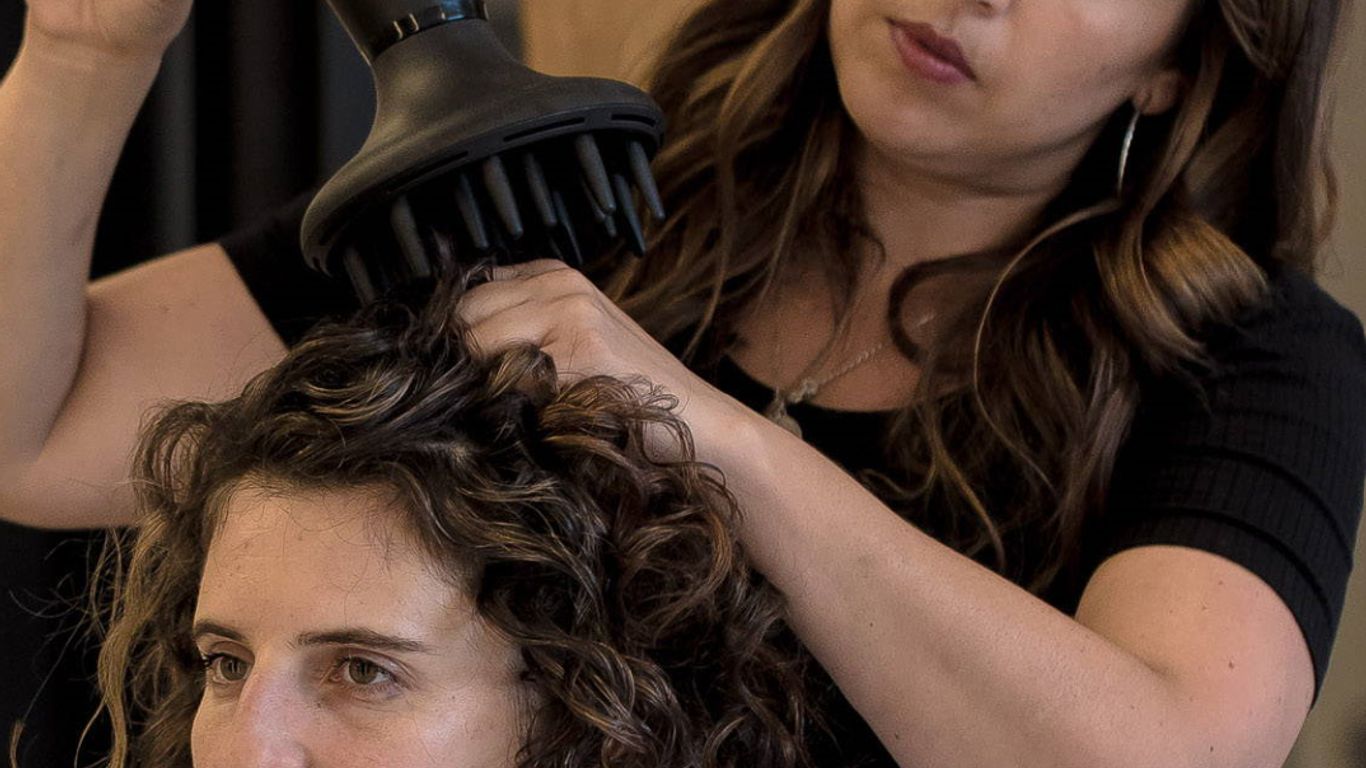 Hair stylist using diffuser on client's curly hair in salon.