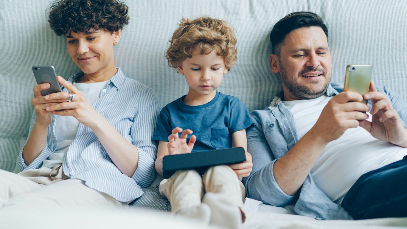 a man, woman and child sitting on a couch looking at their cell phones