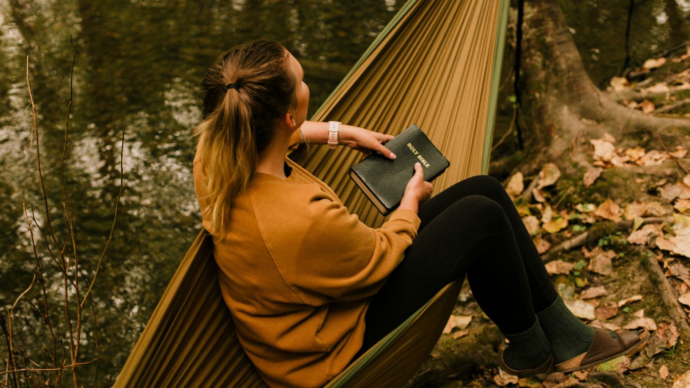 woman in brown coat and black pants sitting on brown wooden bench