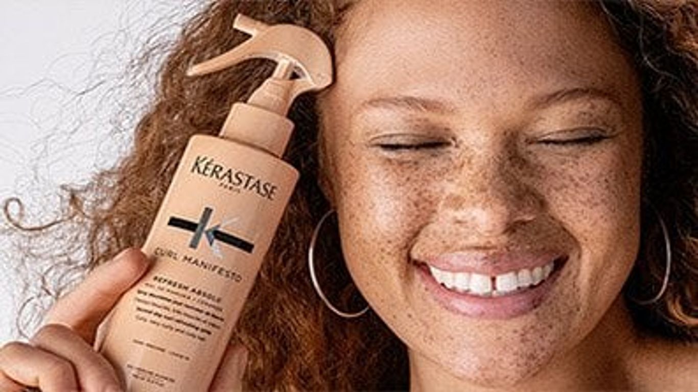 Woman smiling, holding a bottle of haircare product happily.