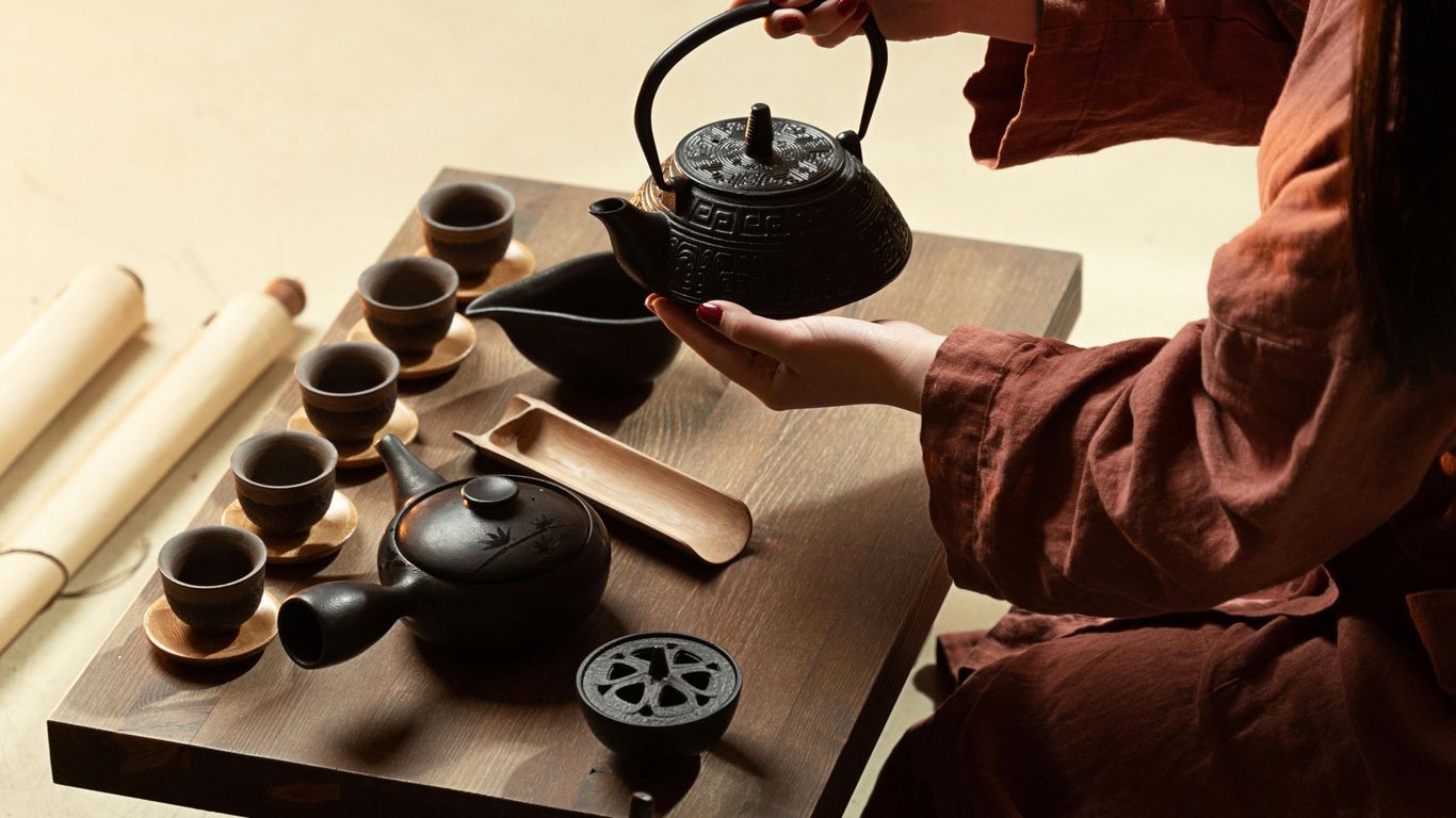 A person performs a traditional tea ceremony with a teapot and cups.