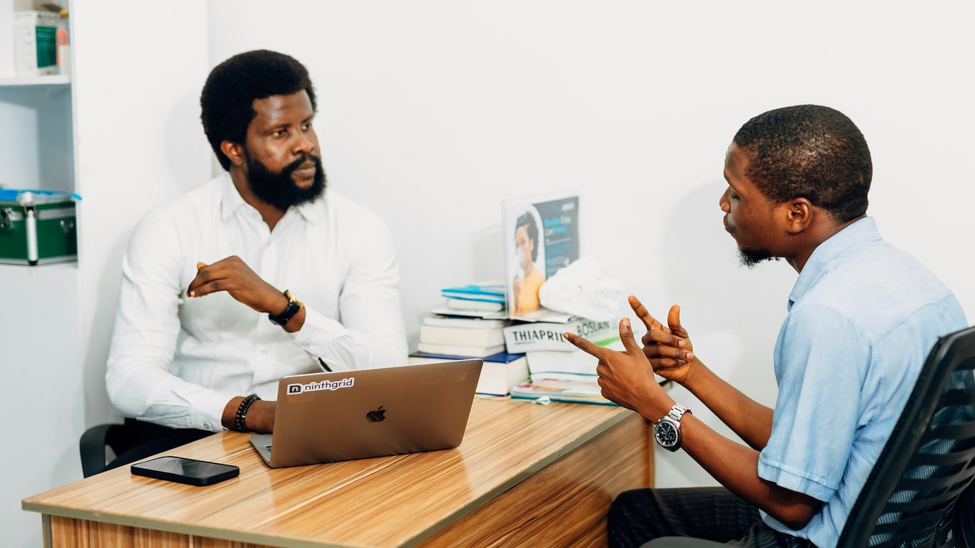 Two men sitting at a desk talking to each other