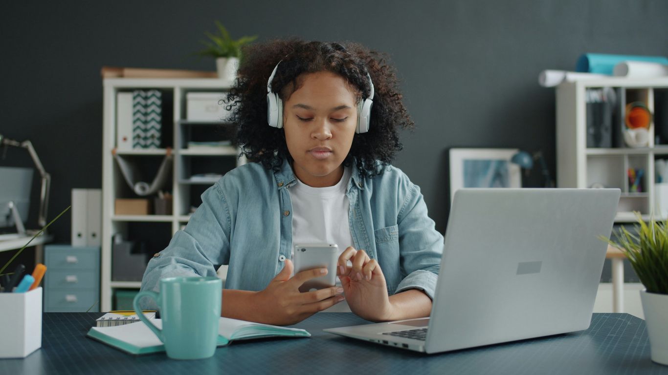 Young girl with headphones uses phone at desk