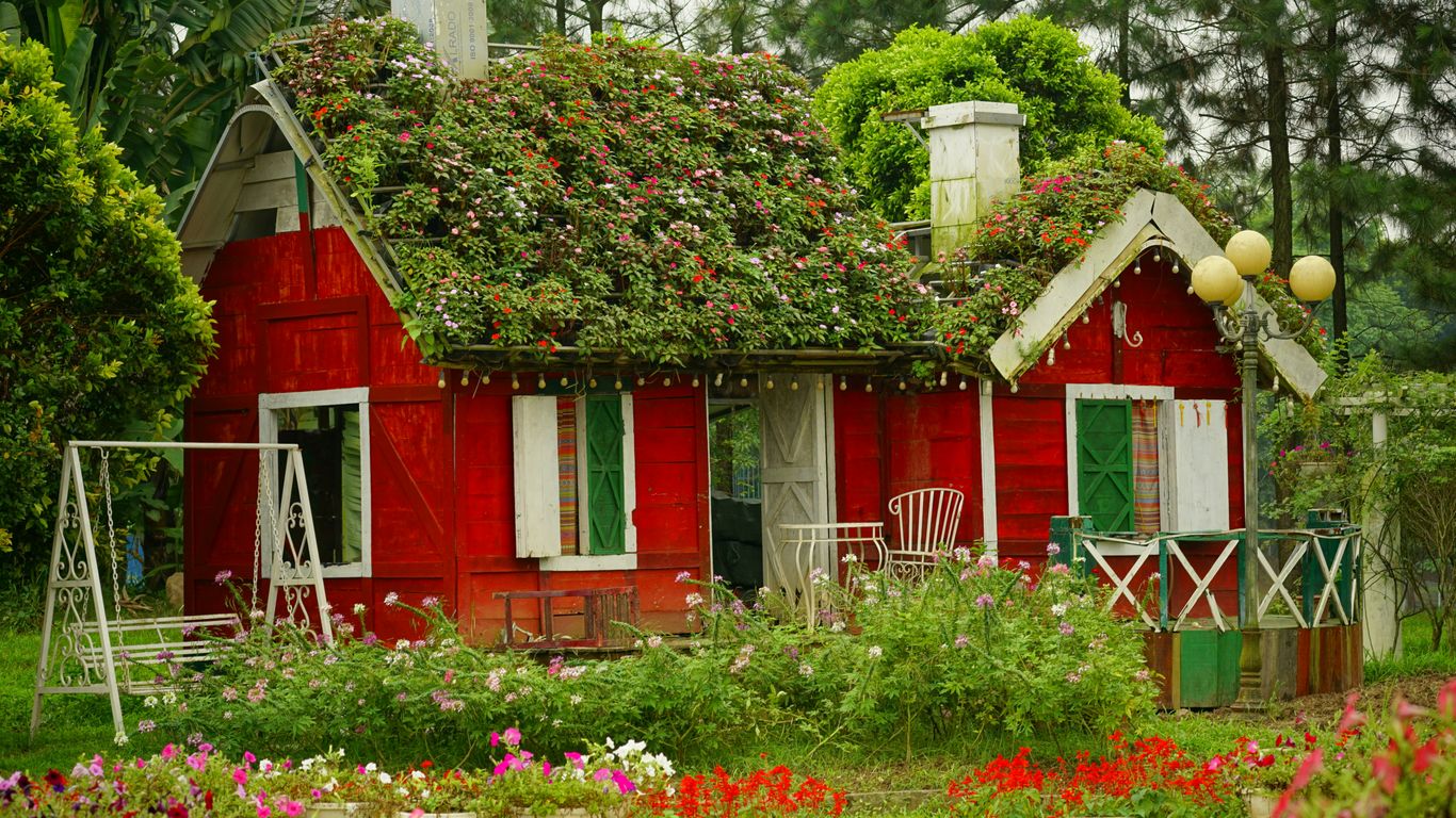a red house with a green roof surrounded by flowers