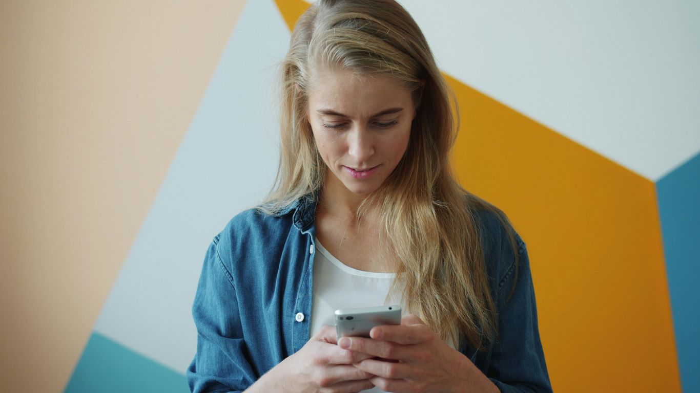 Young woman looking at her phone with a colorful wall.