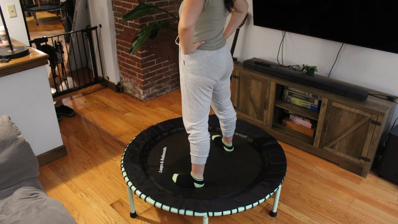 Person standing on indoor trampoline in living room, hands on hips.