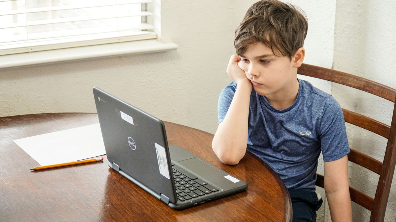 boy in blue crew neck t-shirt using macbook pro on brown wooden table