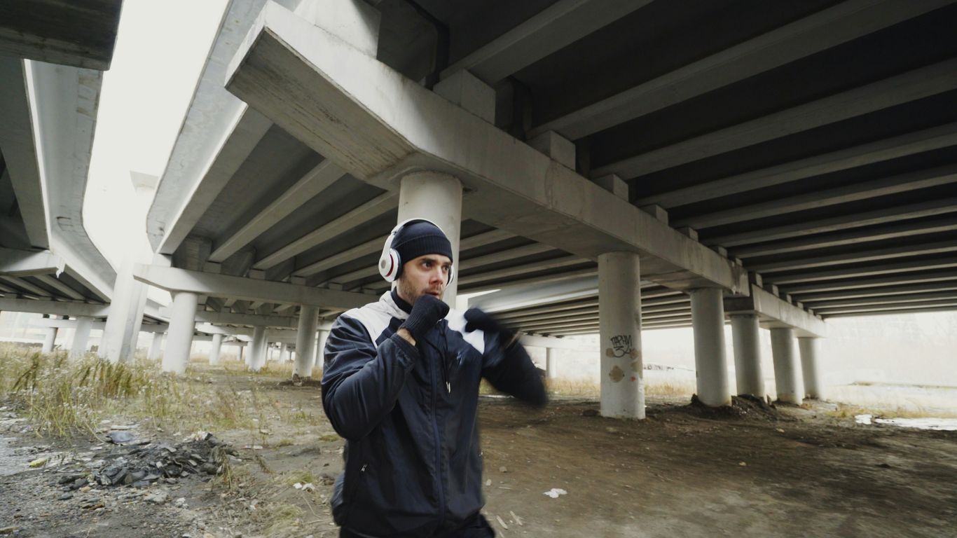 Man with headphones boxing under a bridge