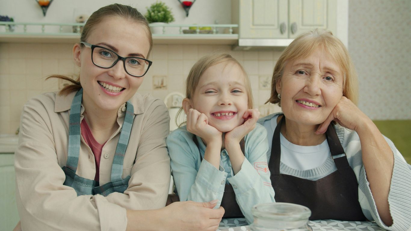 Three smiling women of different ages in a kitchen.