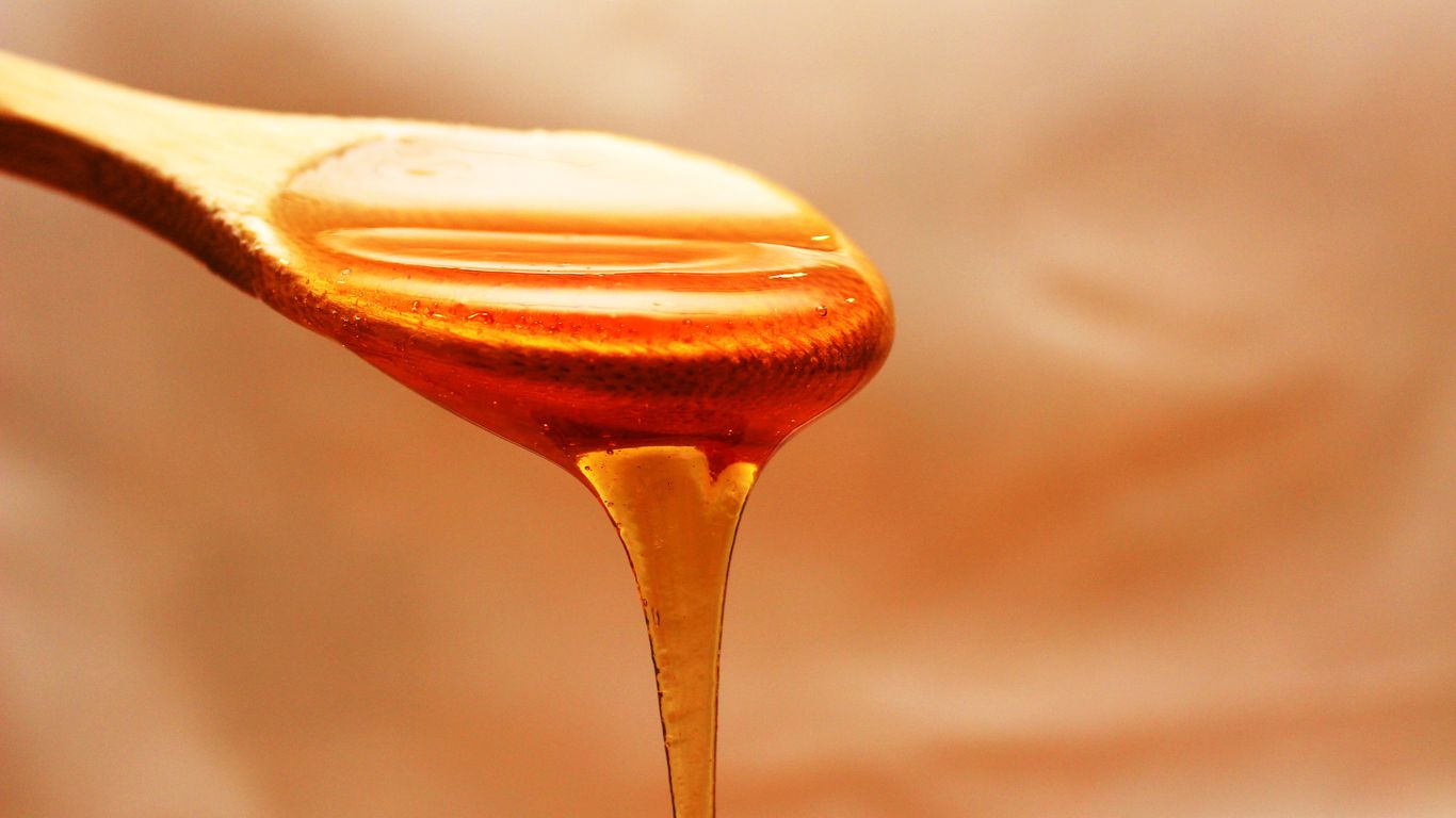 Honey dripping from a wooden spoon against soft background.