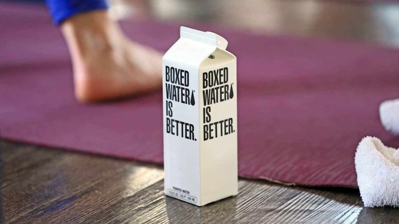 A Boxed Water carton in the foreground with a woman doing yoga in the background