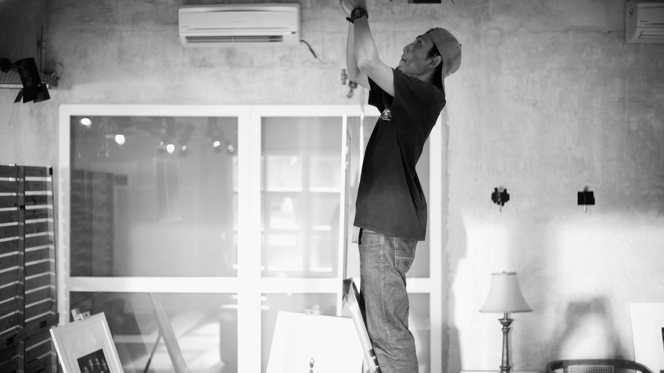 Electrician works on wiring from a ladder indoors.