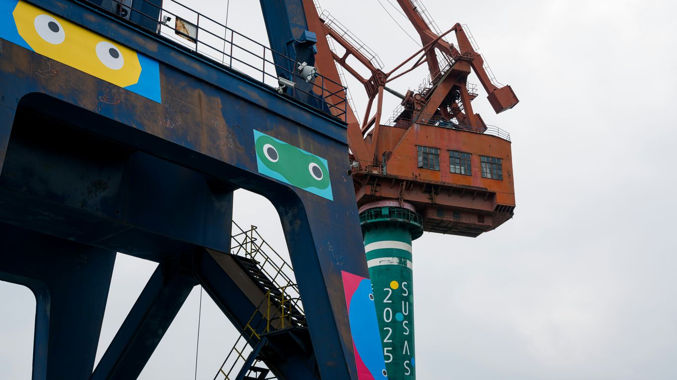Two industrial cranes with colorful cartoon eyes painted on them.