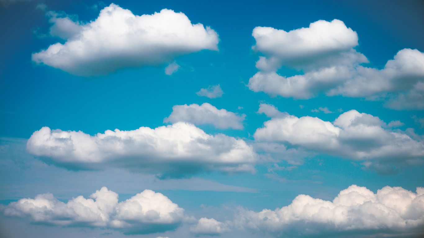 Fluffy white clouds drift across a bright blue sky.