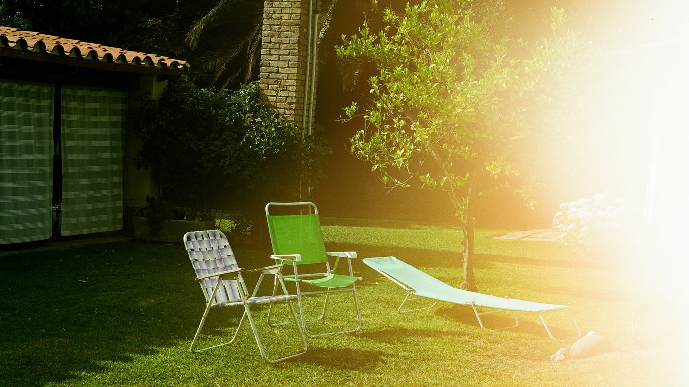 Lawn chairs and lounge on green grass near house.