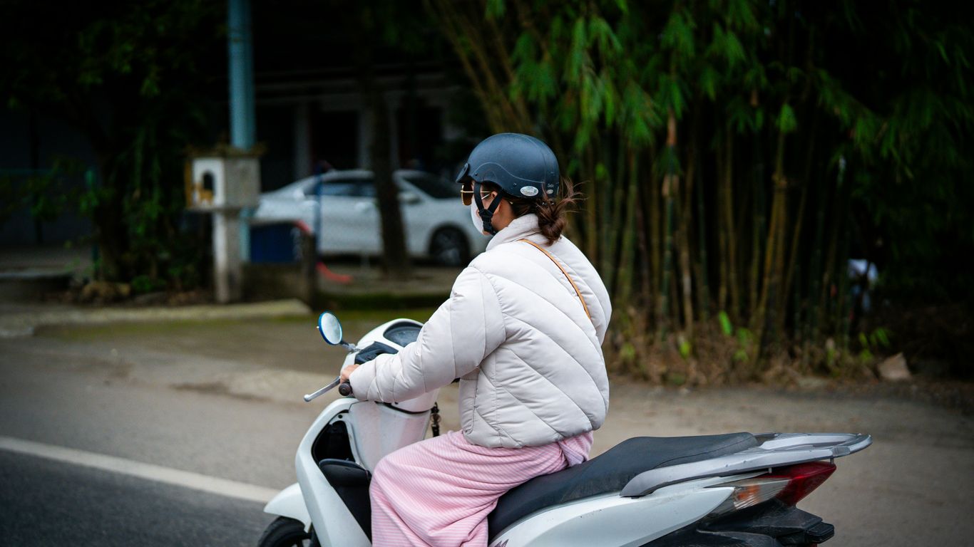 A woman rides a scooter down a road.