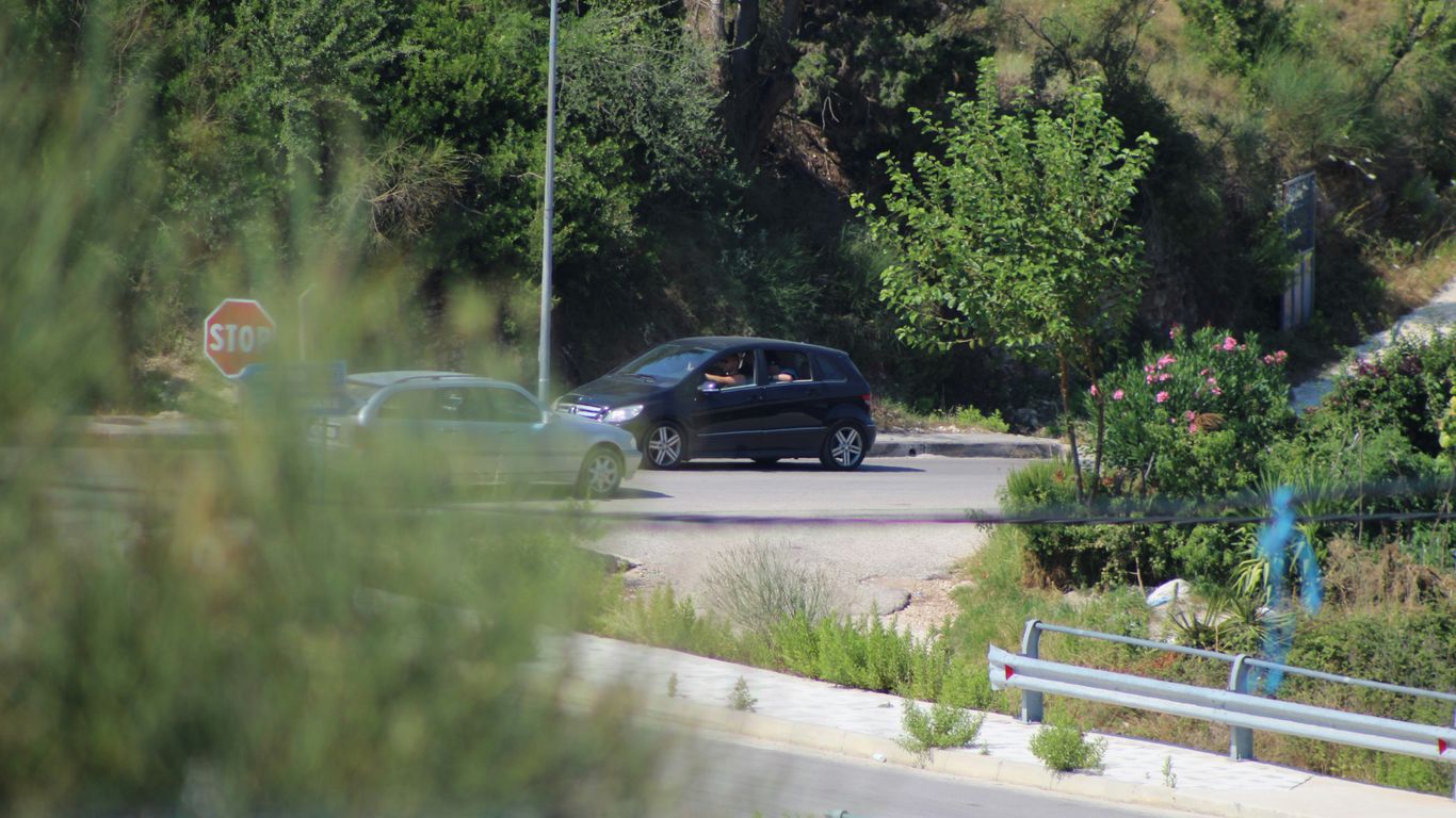a black car driving down a road next to a forest