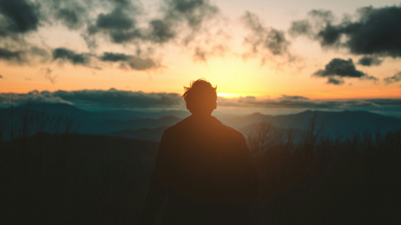 silhouette of man standing on mountain during sunset