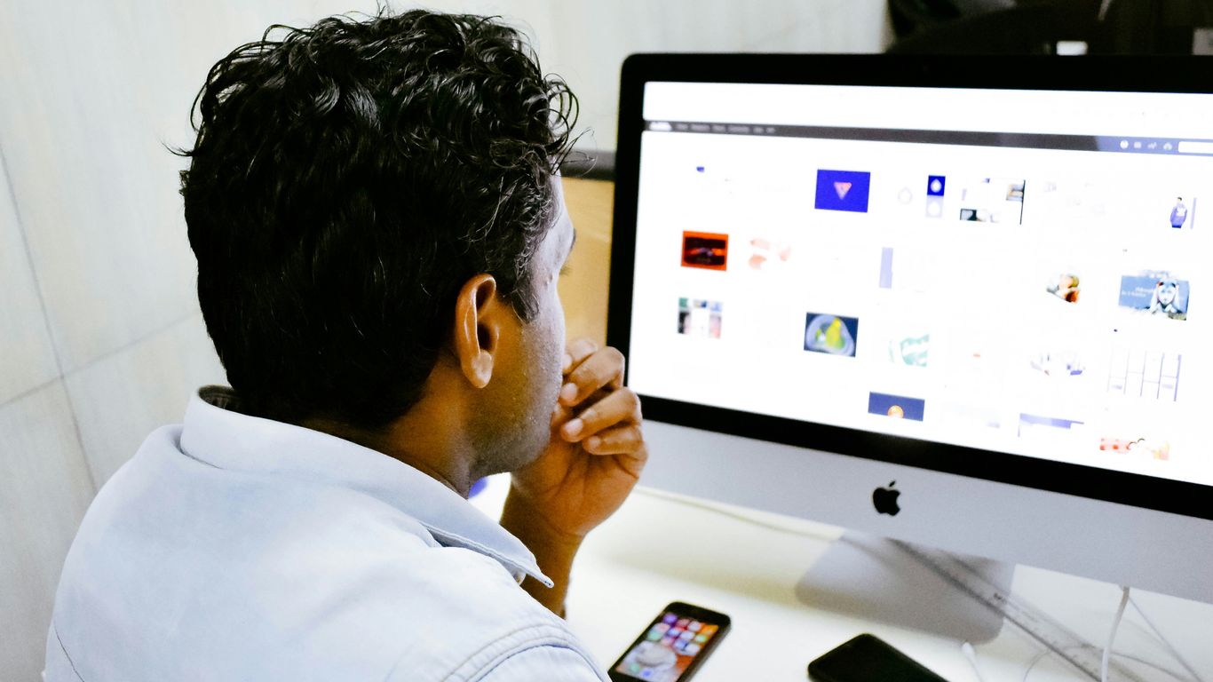man sitting in front of silver Apple iMac on table