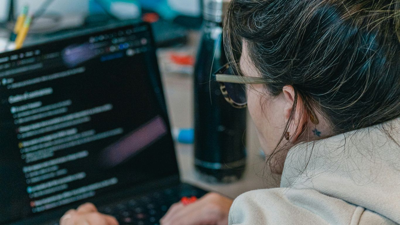 Woman working on a laptop with code on screen.