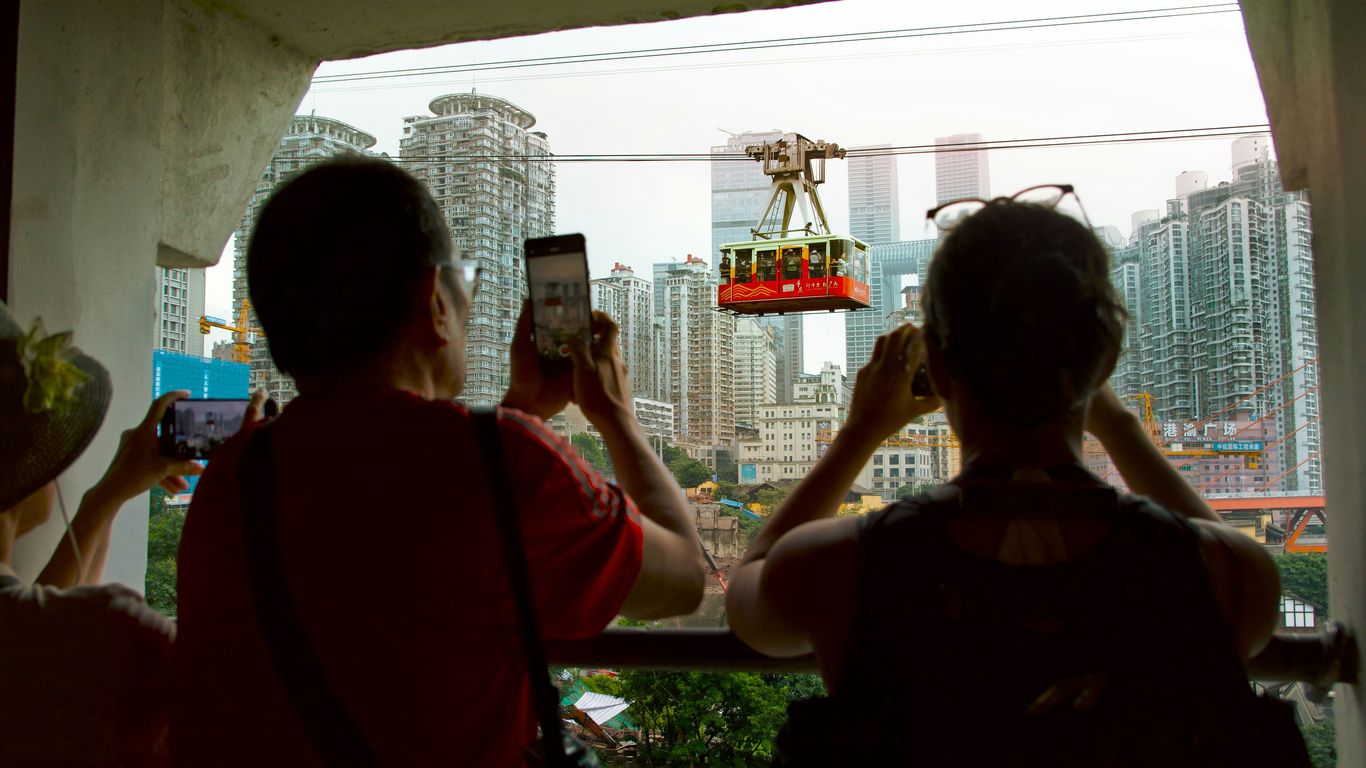 People taking photos of a cable car with city background.