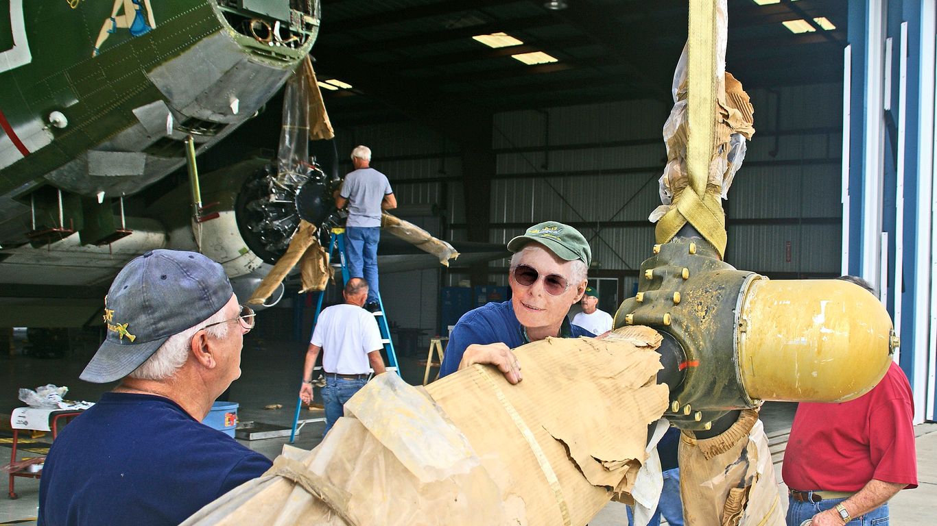 People are working on a vintage airplane's propeller.