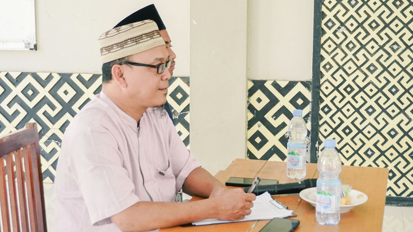 Man wearing a cap and glasses writes at table.