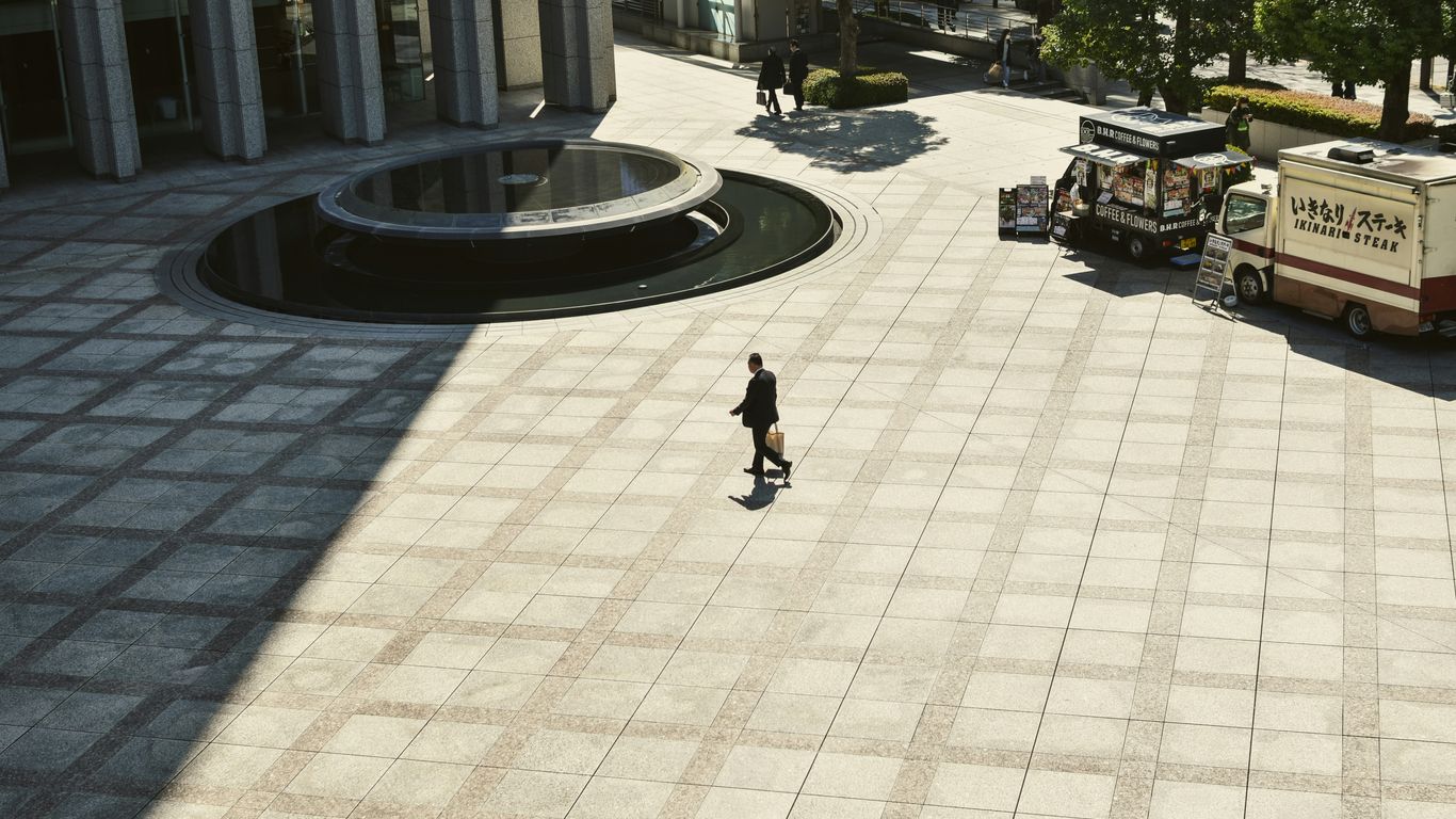 A person walks across a large, empty plaza.