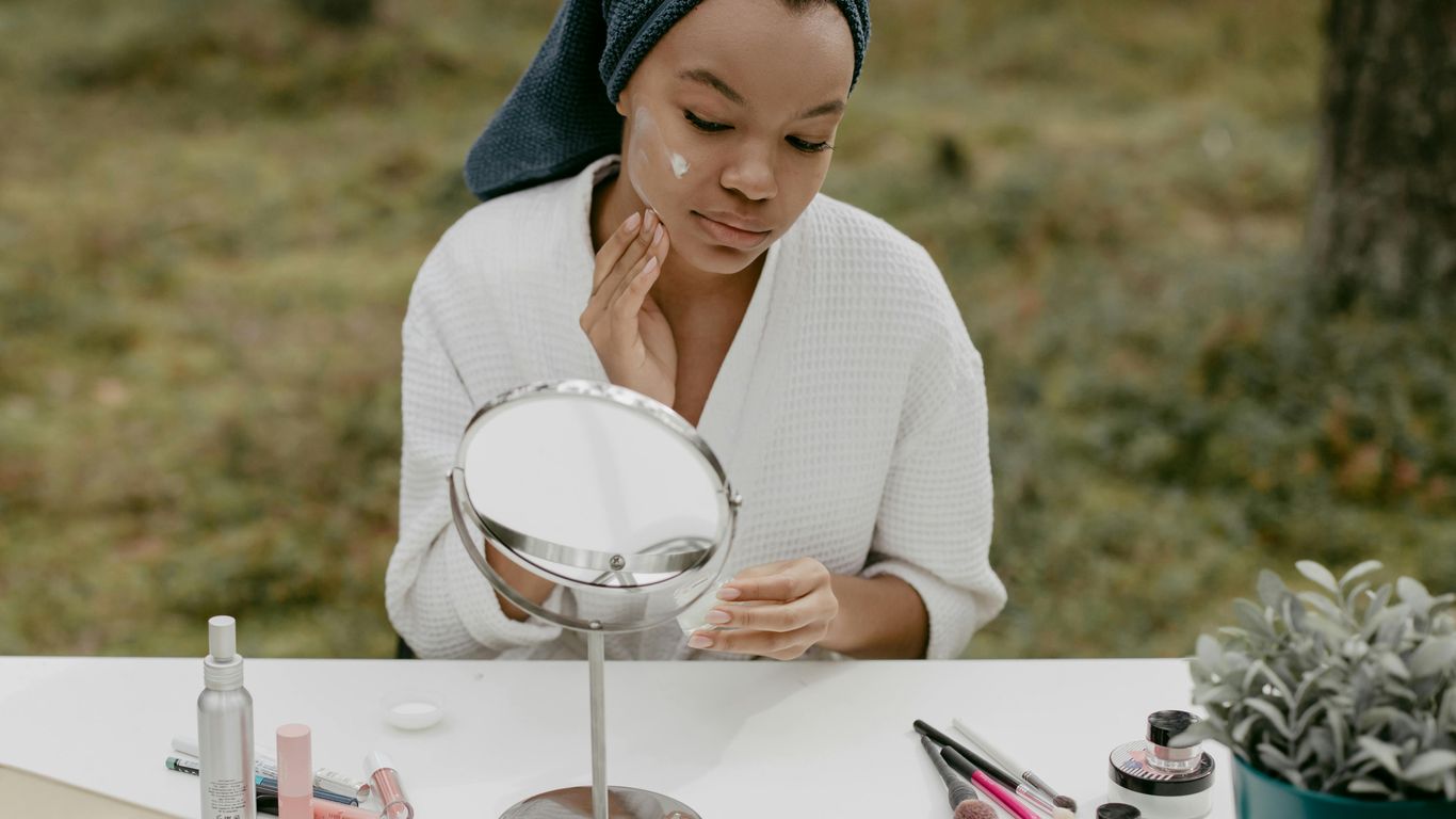 Person applying skincare at a table with beauty products outdoors.