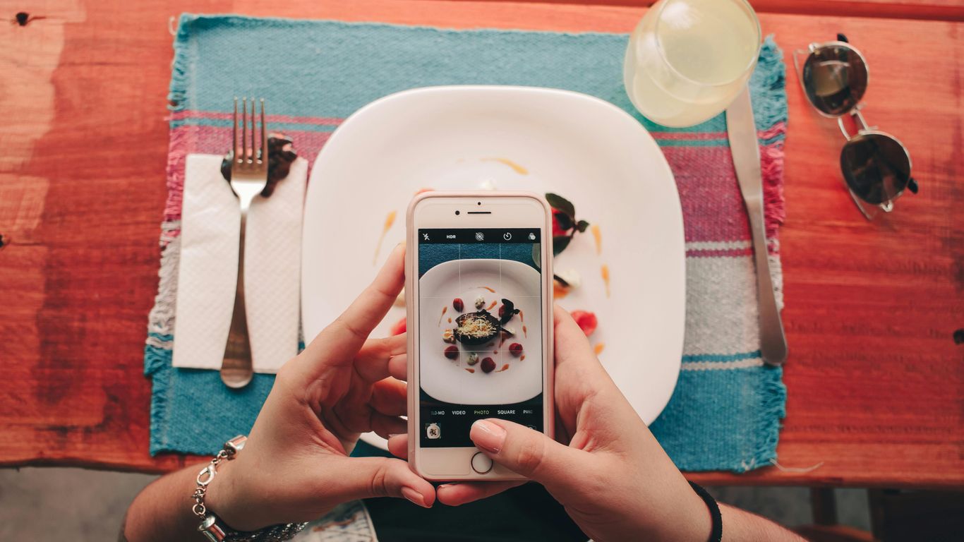 Person taking a photo of food with a smartphone at table.