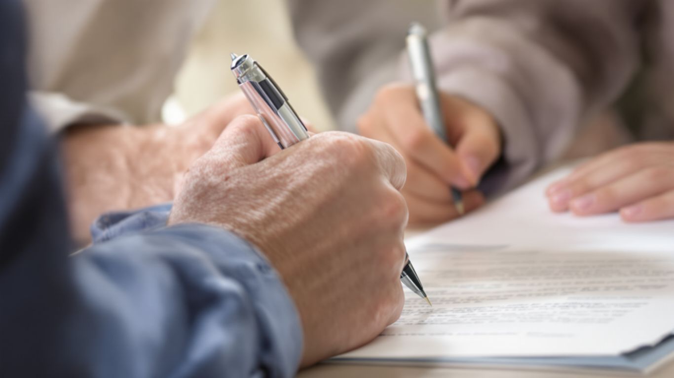 Hands signing a document with a pen.