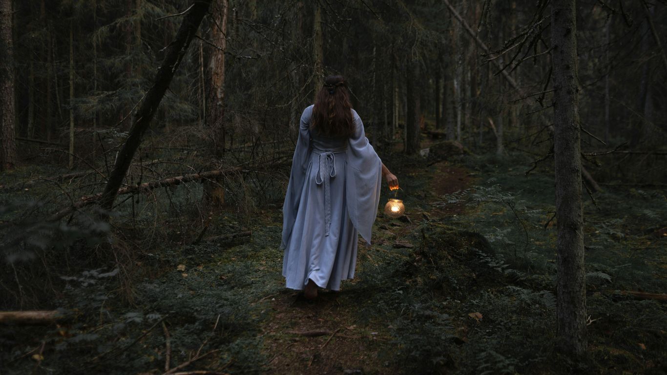a woman dressed as a ghost walking through a forest