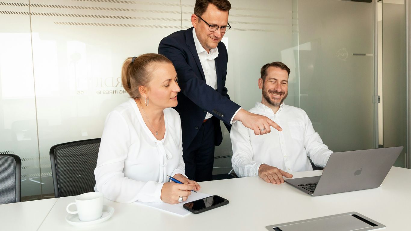 Three colleagues collaborating around a laptop in a meeting room.