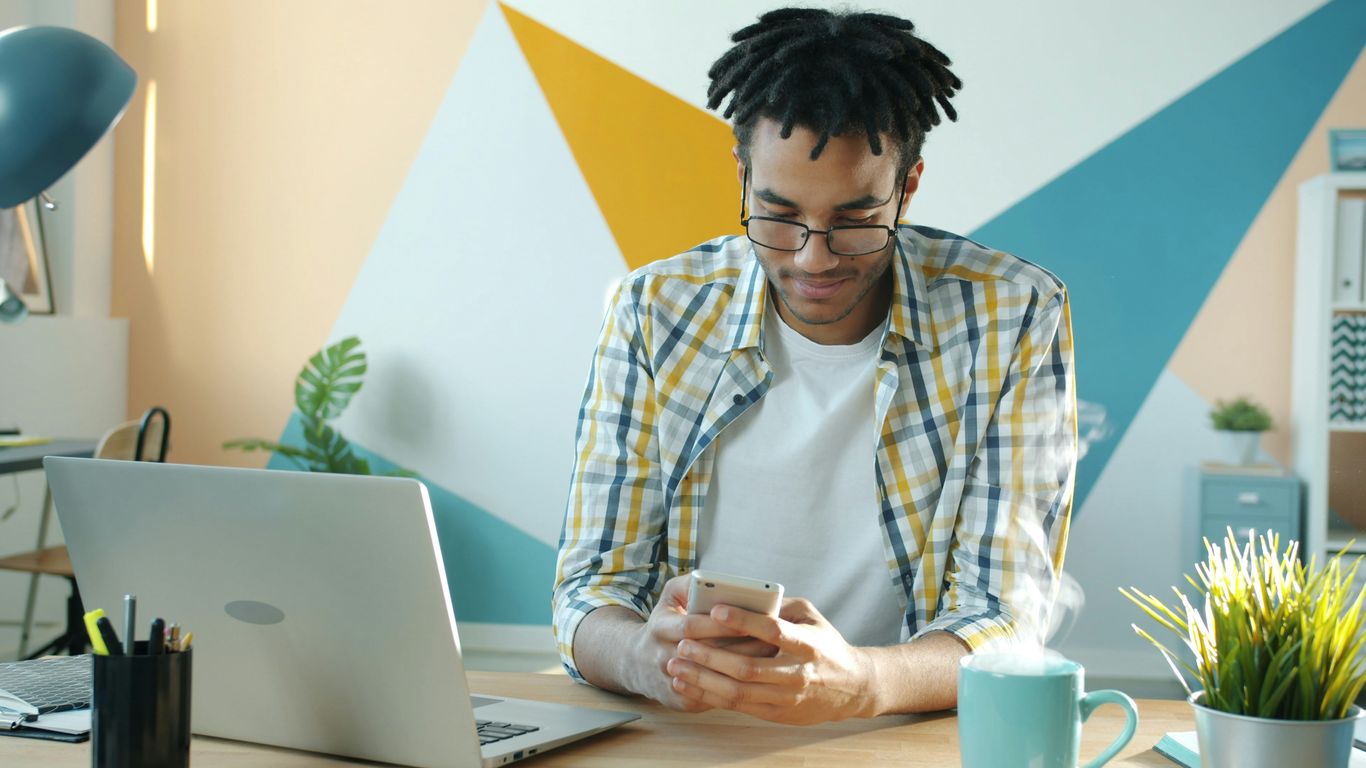 Man in plaid shirt using smartphone at desk