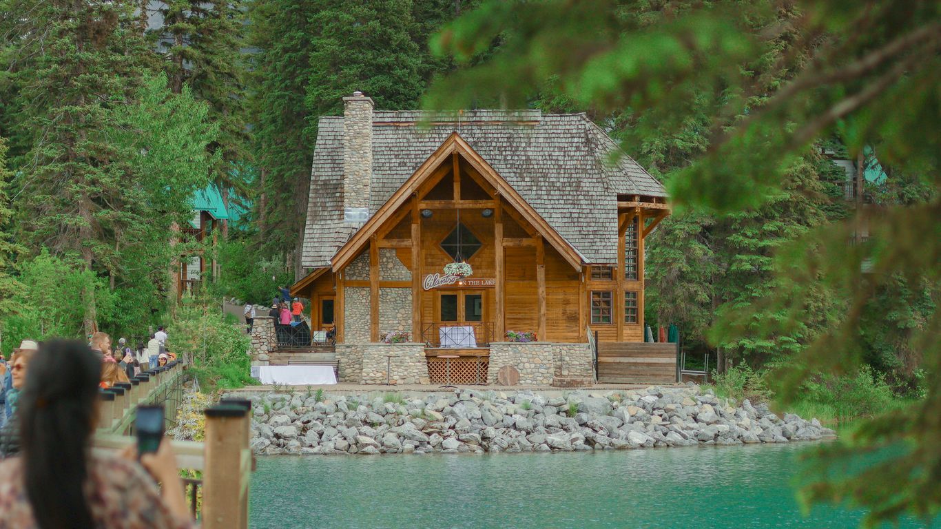 A wooden cabin sits beside a calm lake.