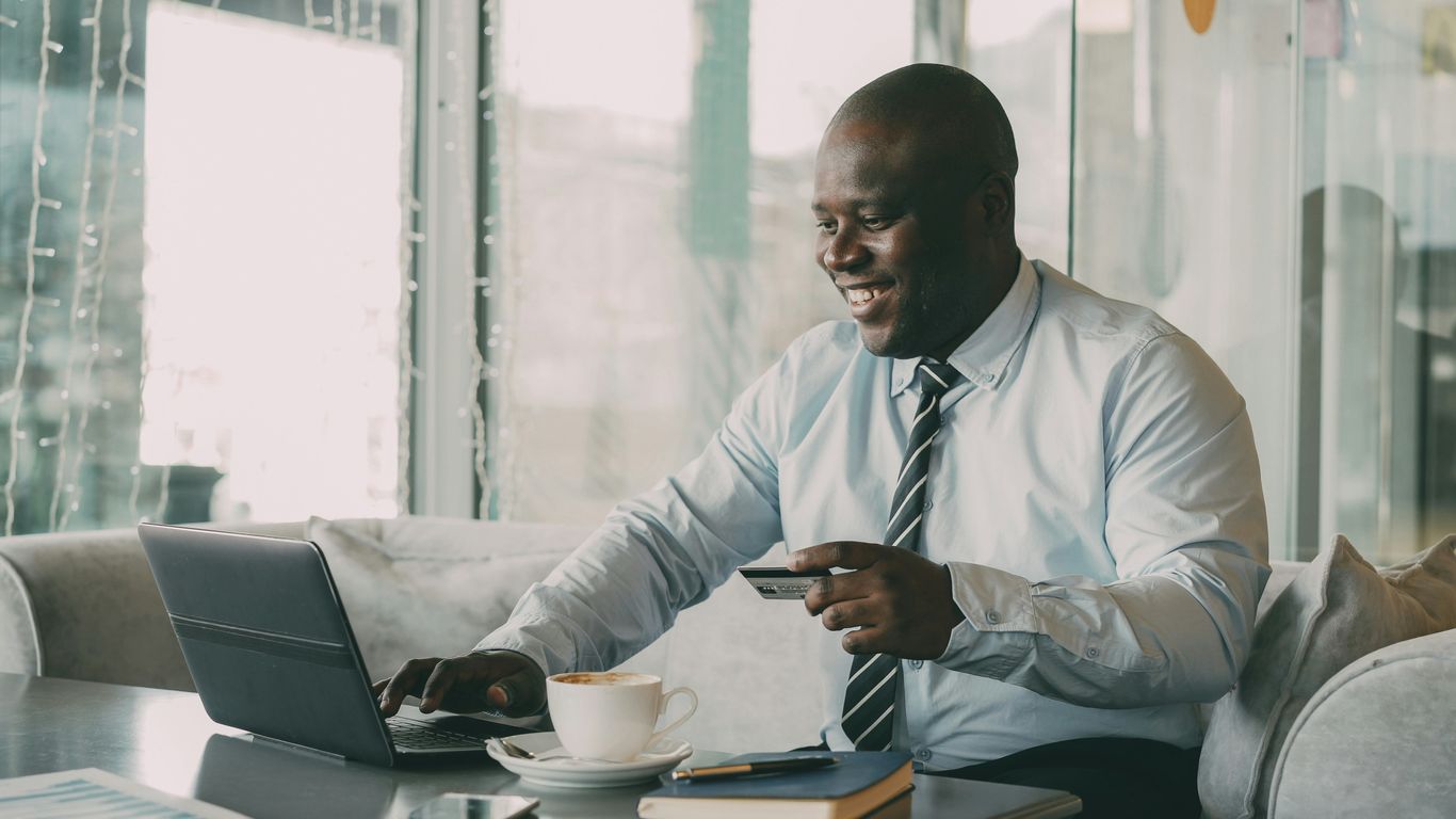 Man with credit card using laptop with coffee.