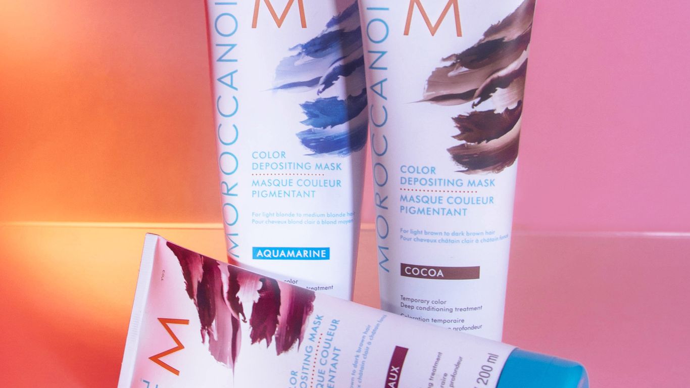 Color depositing masks by Moroccanoil on a pink background.