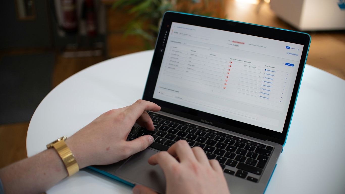 Hands typing on a laptop with a spreadsheet on screen.