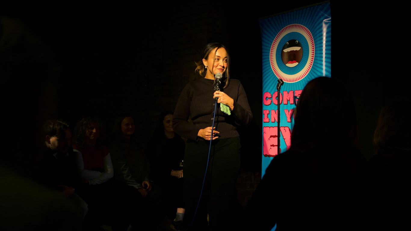 A person performs stand-up comedy on a dimly lit stage.