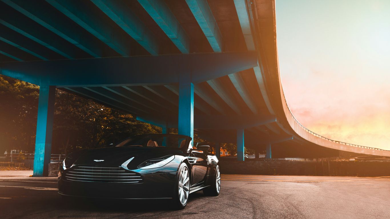 black Aston Martin convertible coupe parked beside blue concrete bridge