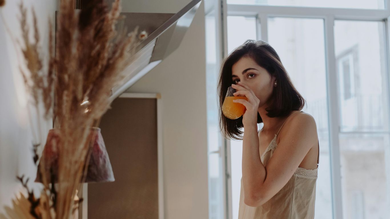Person in a kitchen drinks orange juice, morning light shines in.