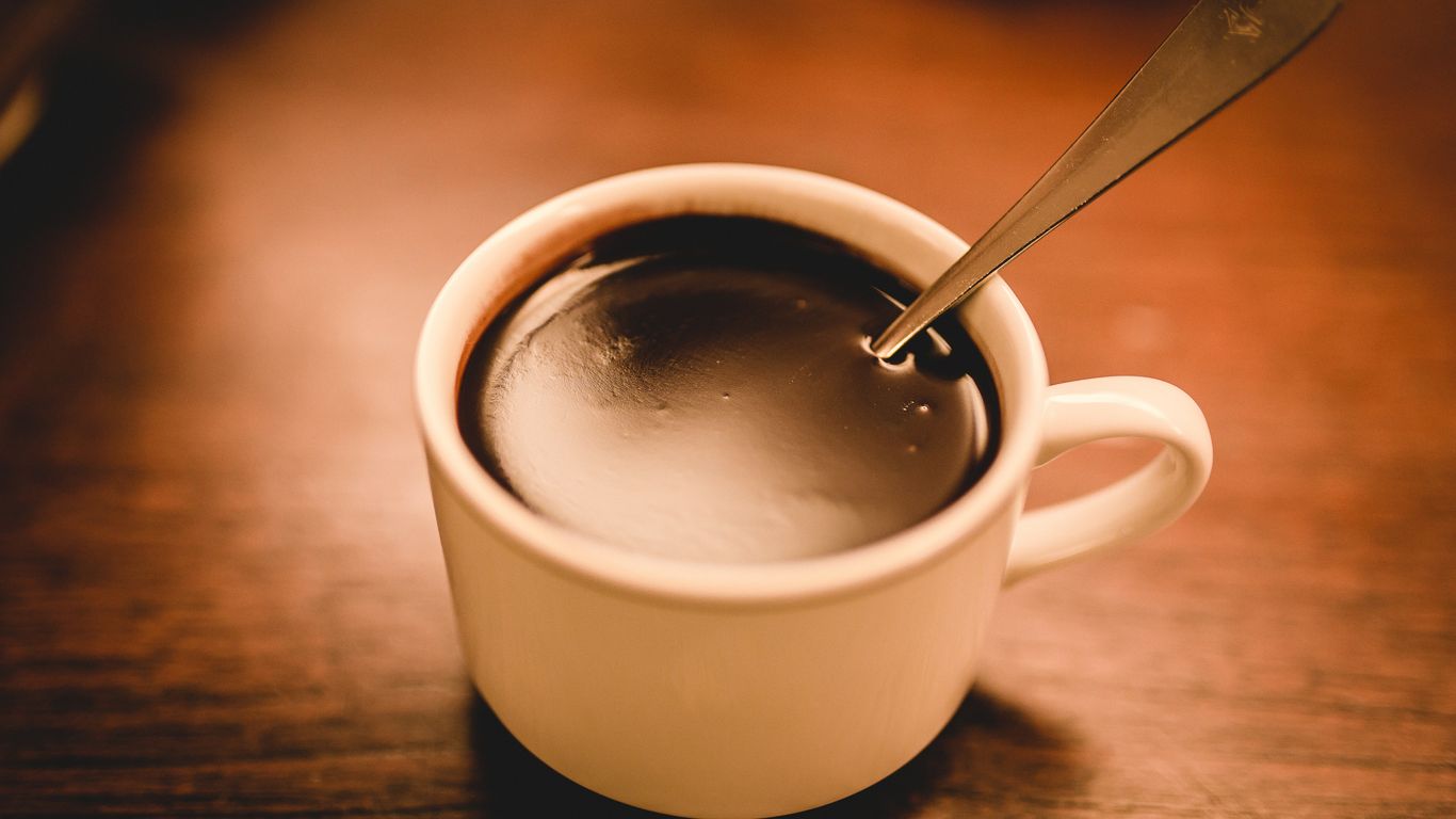 A cup of black coffee with a spoon on table.
