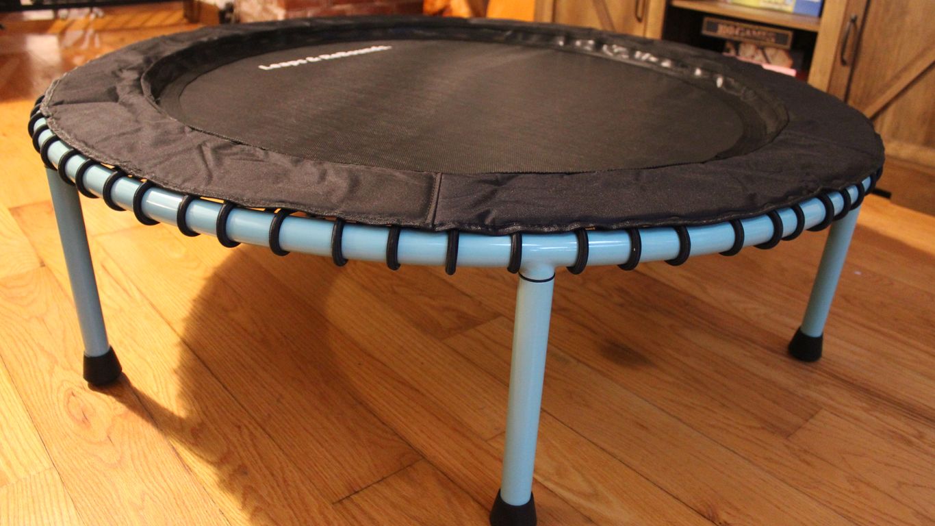 Small indoor trampoline with blue legs on wooden floor.