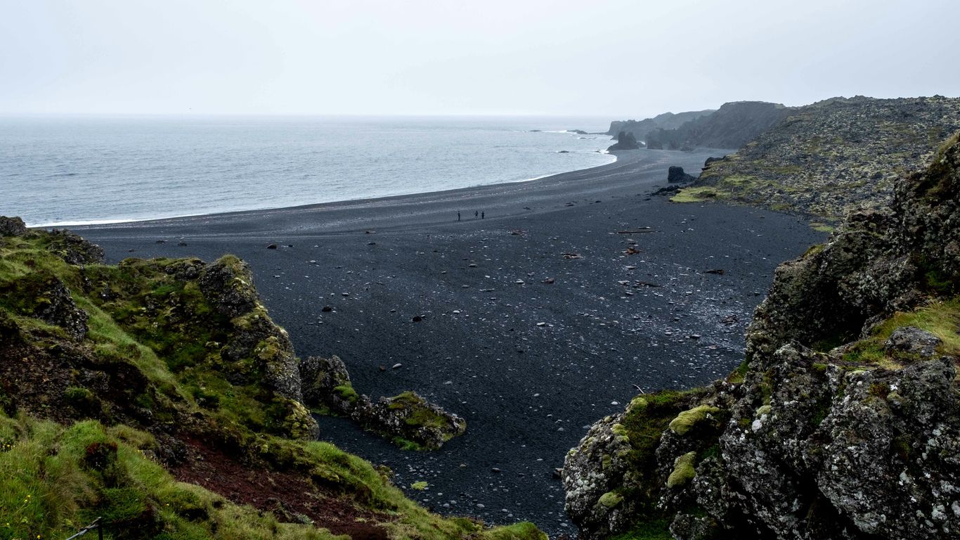 a black sand beach surrounded by green grass