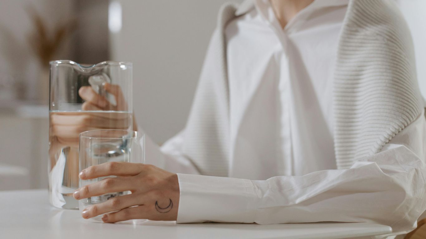 Person holding glass of water, pitcher, crescent moon tattoo visible.