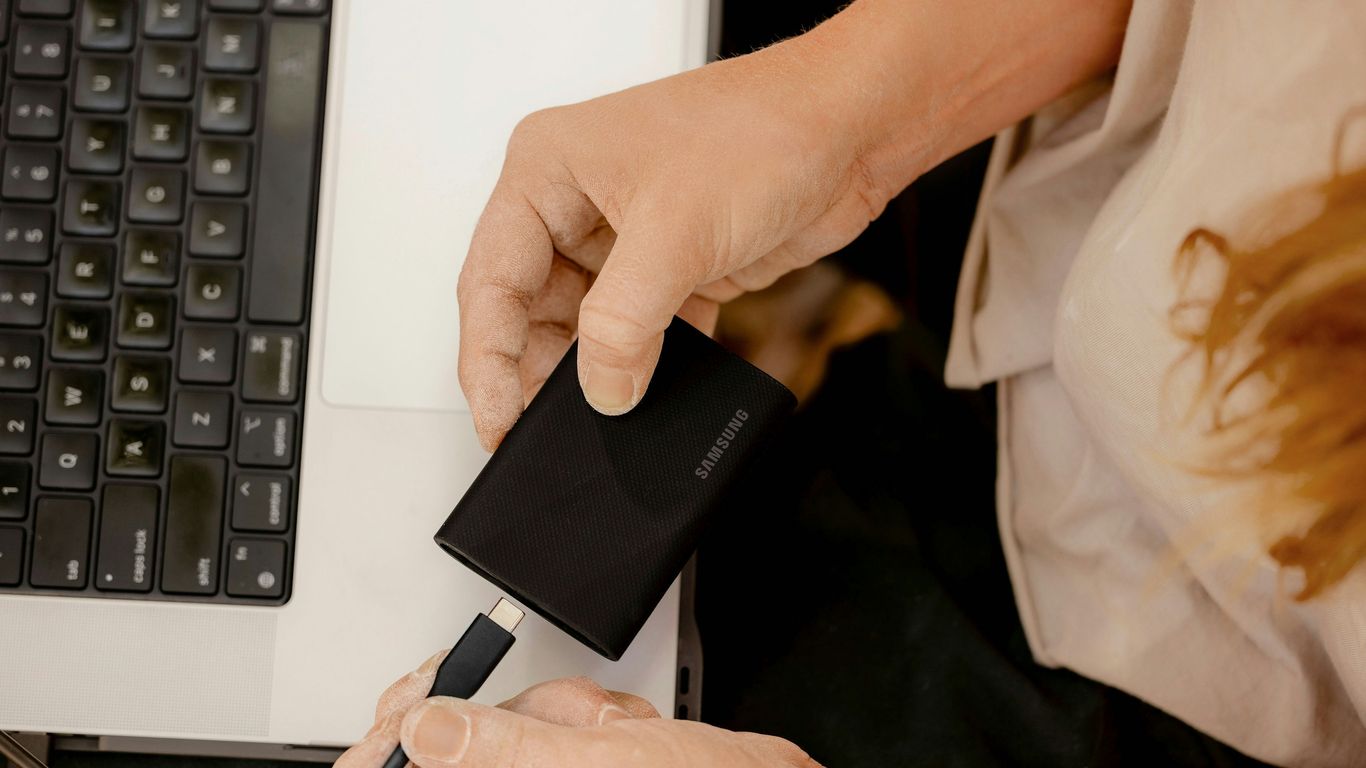A person holding a cell phone in front of a laptop